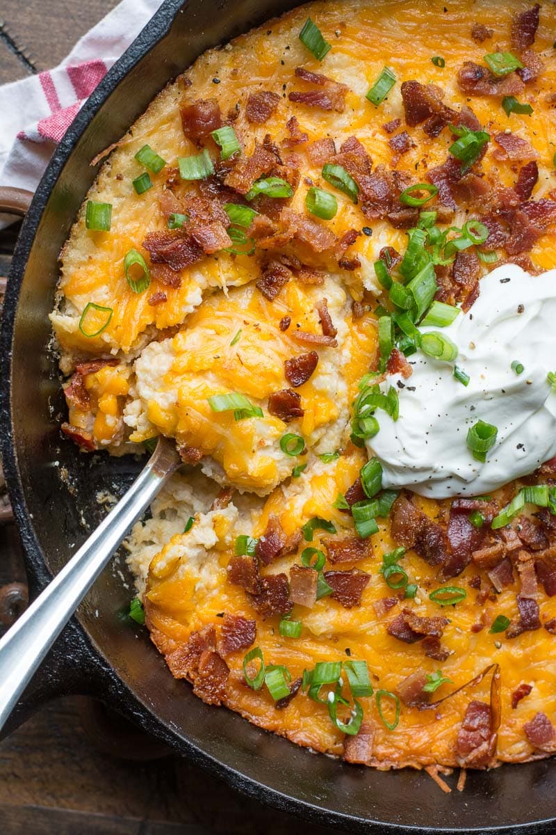 overhead view of cauliflower casserole topped with bacon, green onions, and sour cream