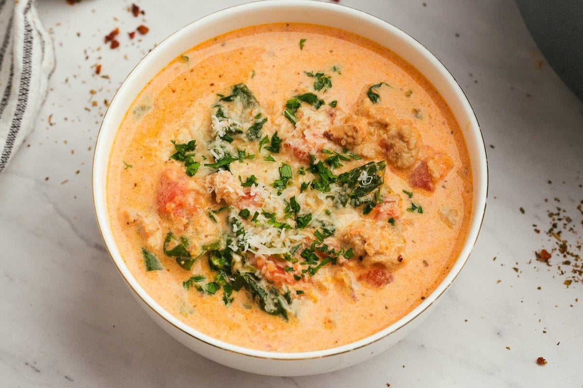 a horizontal image of a white bowl of rich and creamy sausage and spinach soup