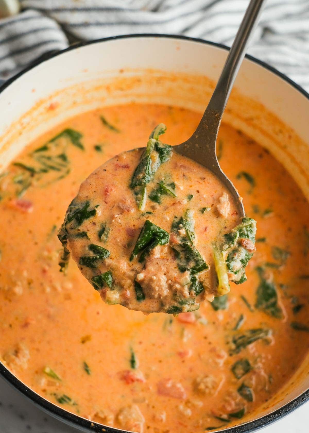 a big ladle full of sausage spinach soup full of tomatoes, cream, and rich broth.